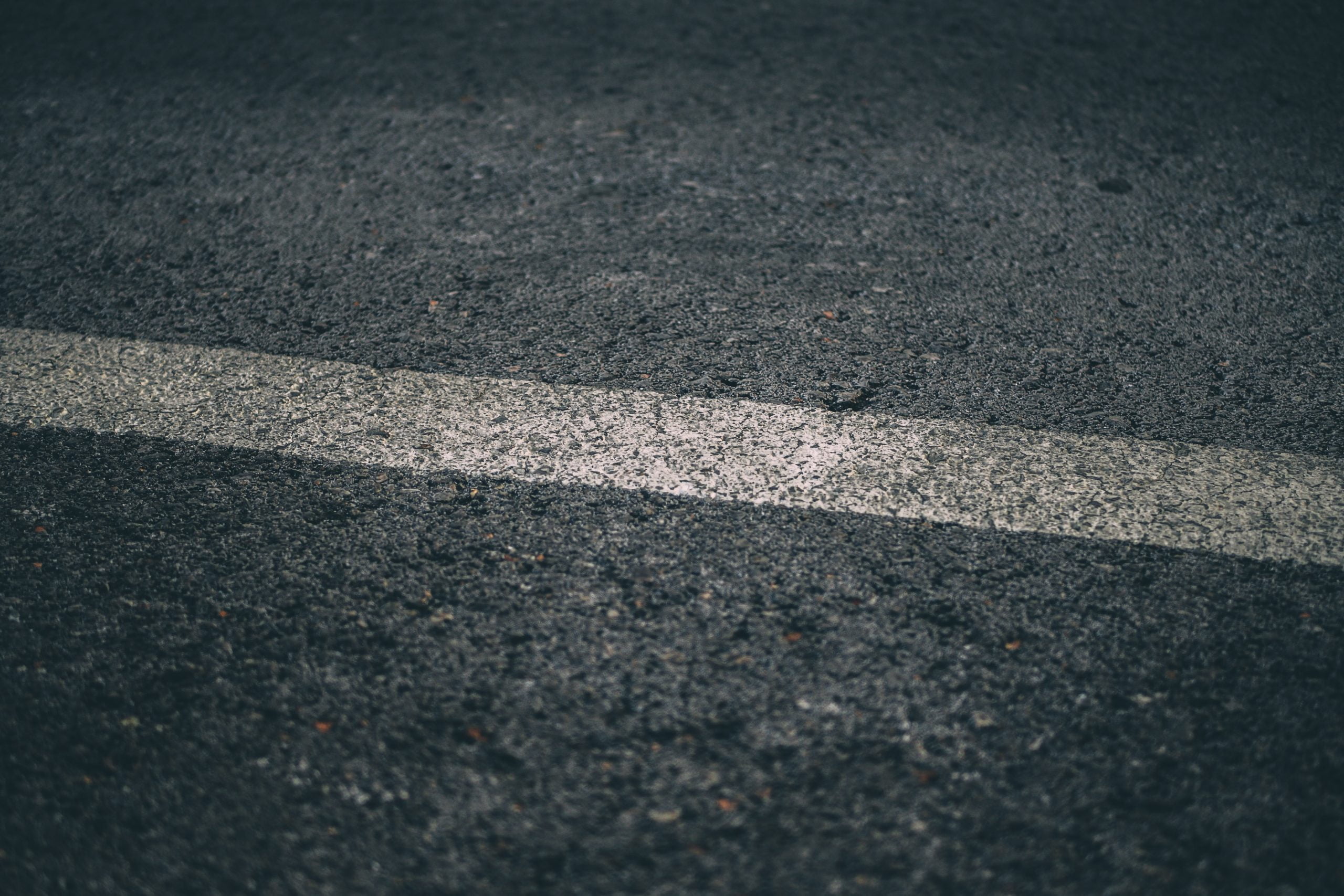 asphalt sealing Close-up of a white line painted on a dark, textured asphalt road.