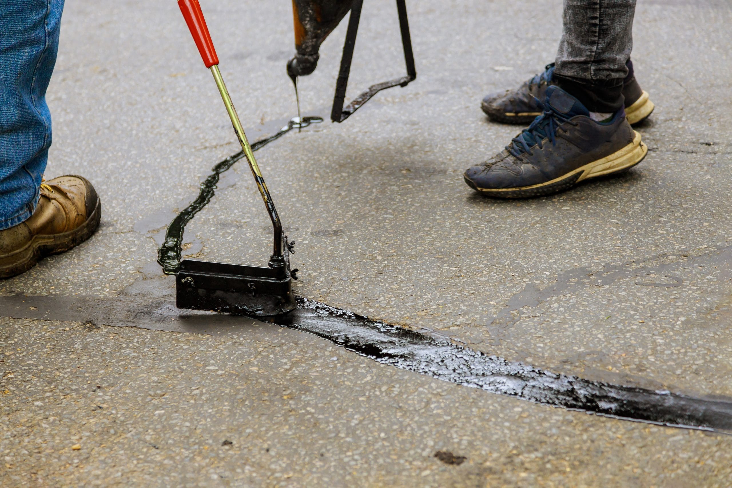 Asphalt road with filled cracks repair, liquid, of the fix road Two workers repair asphalt cracks, sealing them with black sealant and special tools for a smooth, durable finish.
