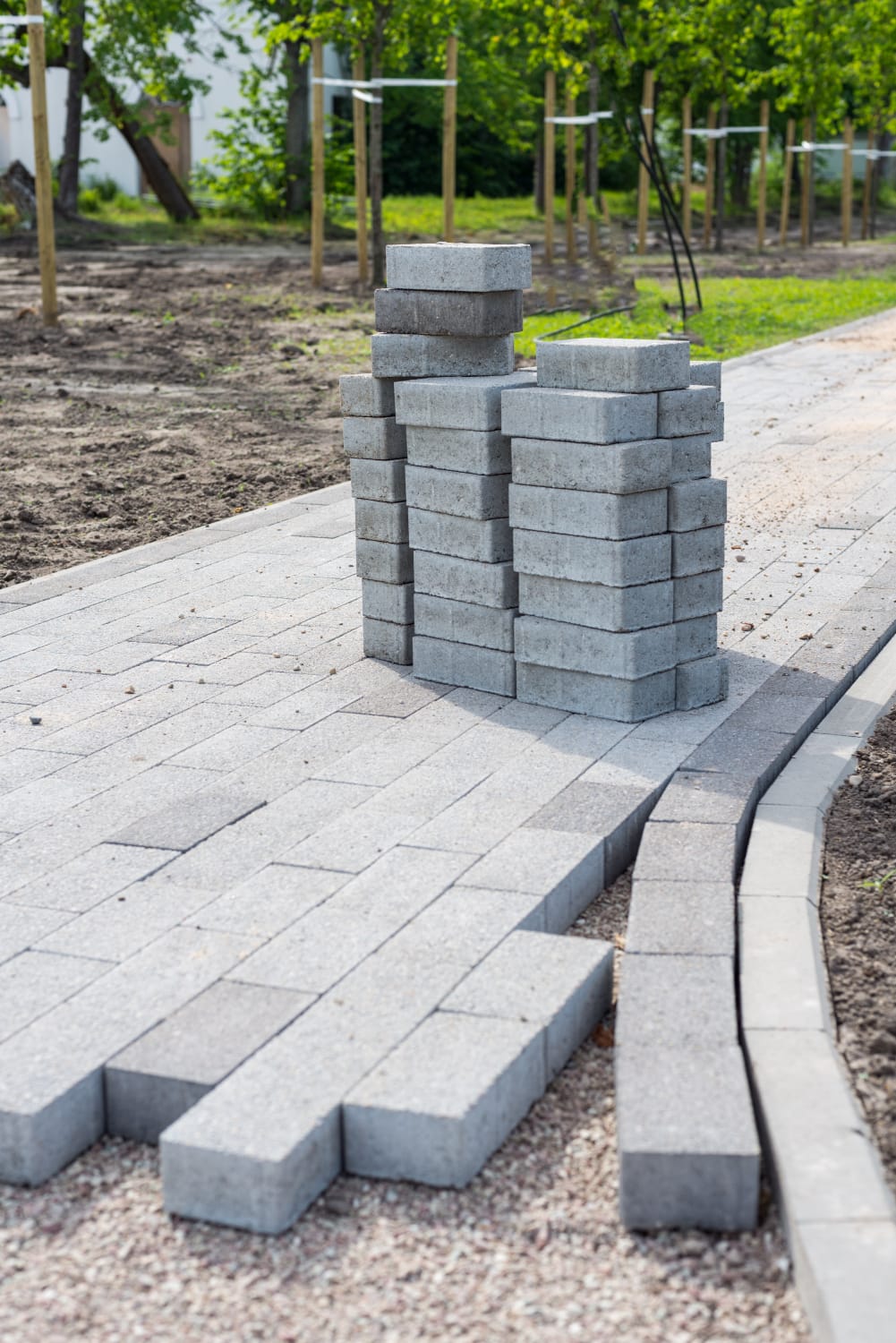 1190 Stacks of gray patio pavers on a partially completed walkway in a garden or park setting.