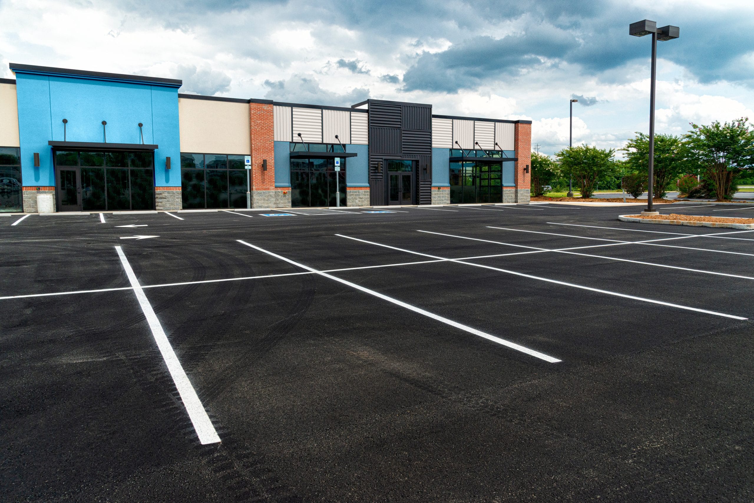 No Customers and Empty Parking Lot at Retail Shopping Center An empty parking lot stretches before a modern, vacant commercial building beneath a cloudy sky.