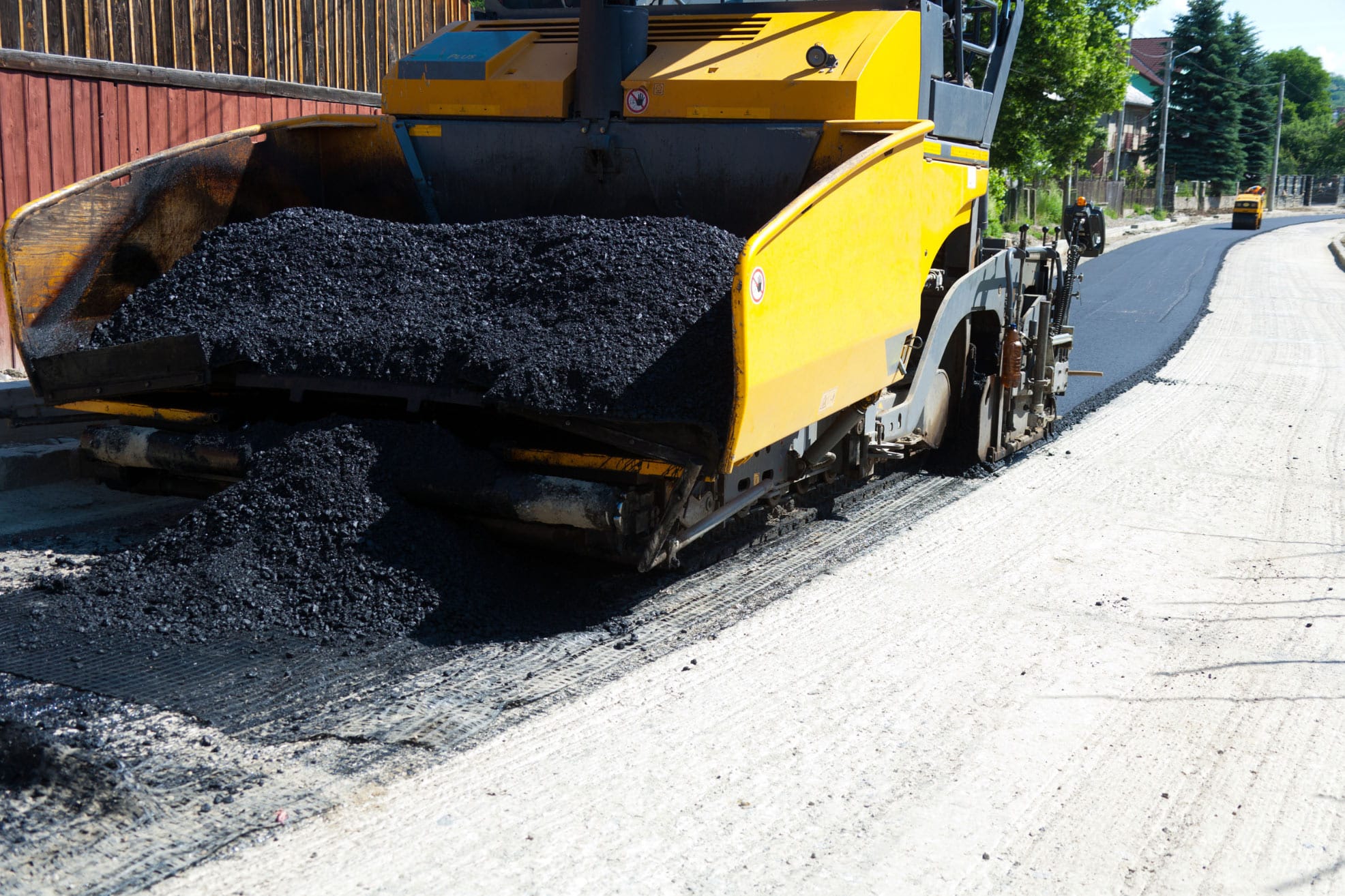 A paving machine spreads fresh asphalt on a road on a sunny day.