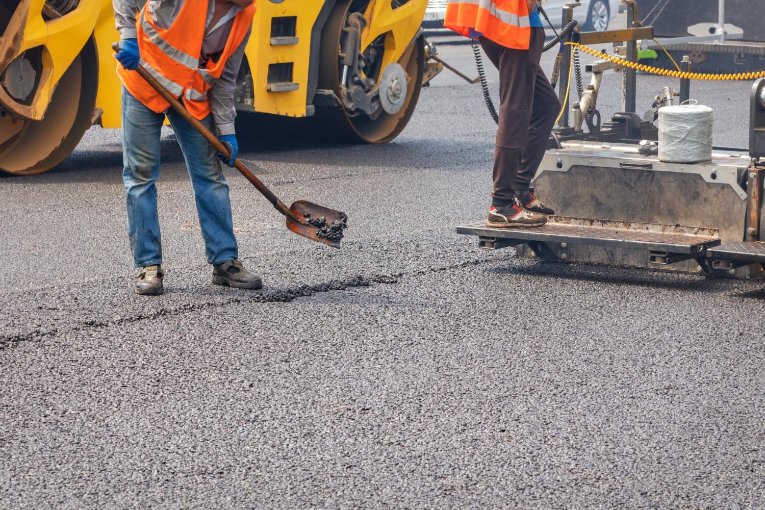 2705941 Workers in safety vests paving a road with asphalt and construction machinery in the background.