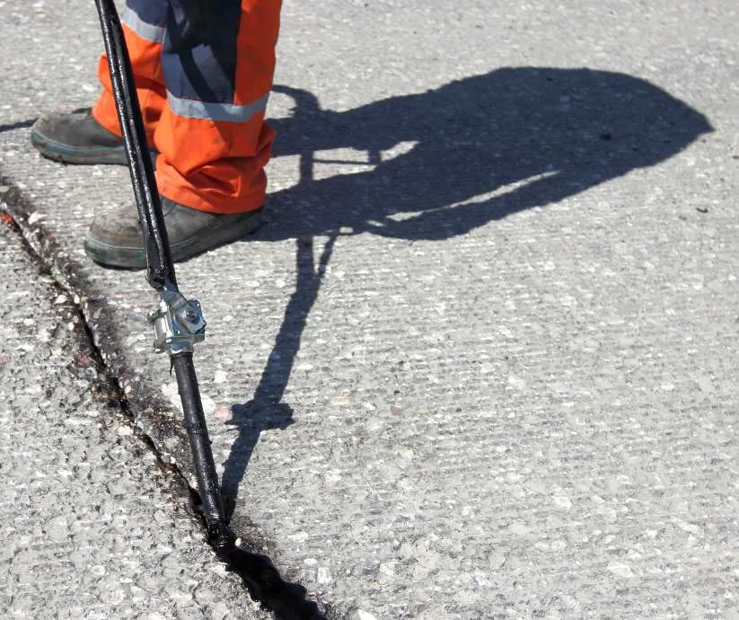 Worker in orange pants sealing a crack in the asphalt using specialized equipment.